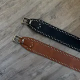 Cinto ancho de cuero negro con hebilla metálica plateada y tachas plateadas.