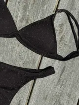 Bikini de dos piezas color marrón, con corpiño triangular fijo con corte bajo el busto, breteles regulables con hebilla y almohadillas desmontables. La bombacha es vedetina con frunce elástico en los costados.