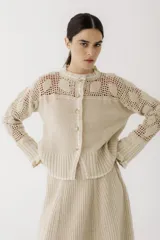 Saco de punto color beige, con diseño de calados en la parte superior y mangas, cierre frontal con botones y cuello redondo.