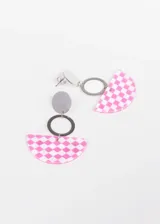 Par de aros colgantes con base de acero quirúrgico, un dije circular plateado, un aro plateado y un dije semicircular de acrílico con estampado a cuadros blancos y negros.