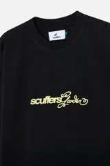 Remera negra de algodón con corte oversize y cuello redondo acanalado. Presenta un estampado grande en la espalda con texto en blanco y amarillo que incluye la palabra "Scuffers", "Garden", "Everyday Urban Aesthetics" y un diseño de flores blancas.