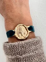 Pulsera dorada con dije redondo con la imagen de la Virgen de Fátima y cinta de terciopelo elástico color verde petróleo.
