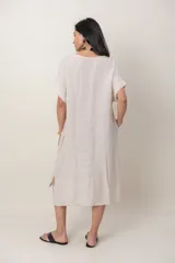 Vestido midi de lino color beige, de corte holgado y silueta acampanada. Cuenta con cuello redondo, mangas cortas amplias, bolsillos laterales y detalles de recortes horizontales en la falda con terminación asimétrica más larga en la parte trasera.