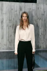 Pantalón de tiro alto en color negro, con diseño de corte recto y ligeramente acampanado. Presenta costuras verticales marcadas en el frente y bolsillos laterales de vivo.
