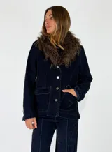 Chaqueta de denim azul oscuro con cuello de piel sintética desmontable, cierre frontal con botones metálicos y bolsillos delanteros con solapa.