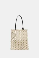 Bolso tipo shopper de tamaño pequeño, tejido en crochet color beige claro con patrón calado. Incluye asas de hombro de cuero sintético marrón oscuro y una bolsa interior con cierre de cremallera.