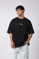 Remera negra de corte oversize confeccionada en tela pesada. Presenta un bordado frontal con la palabra 'REWIND' y un diseño de parche en la espalda con estética de papel roto.