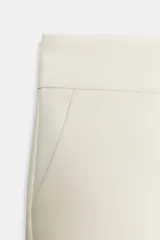 Shorts de tiro medio color crema, con bolsillos laterales y falsos bolsillos con solapa en la parte trasera. Cierre frontal con cremallera y ganchos metálicos.