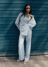 Camisa de popelina celeste a rayas, de corte oversize, con cuello camisero, mangas largas y aplicaciones de pedrería y lentejuelas brillantes distribuidas por toda la prenda.