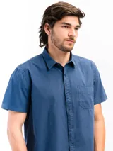 Camisa de manga corta color celeste claro, confeccionada en algodón, con cuello clásico y un bolsillo de parche en el lado izquierdo del pecho.