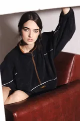 Buzo negro de pana con cuello alto y cierre marrón. Tiene bolsillo delantero con cierre, puños ajustados y ruedo regulable.