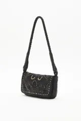 Cartera de mano tipo baguette confeccionada en cuero vacuno negro, con solapa decorada mediante diseño calado y tachas metálicas. Presenta una correa trenzada y un pañuelo estampado anudado en uno de sus laterales.