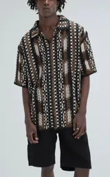 Camisa de manga corta tejida en punto abierto (símil crochet), con calce oversize. Presenta un patrón geométrico en tonos negro, marrón y blanco.