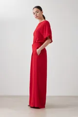 Pantalón palazzo rojo de tiro alto con pliegues marcados en la parte delantera y corte ancho y fluido. La modelo viste un conjunto monocromático con una blusa de manga corta a juego.