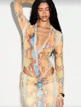 Vestido largo de silueta ajustada con estampado de piel de serpiente en tonos cálidos. Presenta escote profundo con cuello tipo camisa, mangas largas y recortes laterales cut-out que estilizan la figura.