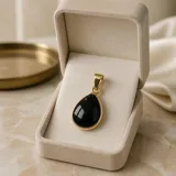 Dije en forma de gota con piedra de onix negra engarzada en acero dorado.