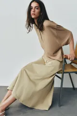 Falda midi de tiro alto color beige, con bolsillos delanteros, cintura con trabillas y cierre frontal con cremallera y ganchos metálicos.