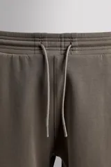 Pantalón jogger de entrenamiento, corte regular fit, color verde oliva oscuro. Confeccionado en tejido técnico compacto de algodón con elasticidad y efecto neopreno. Presenta cintura elástica ajustable con cordón blanco, bolsillos frontales y un bolsillo lateral con cierre de cremallera. El bajo termina en puño.