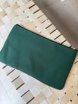 Sobre tipo cartuchera de lona naranja con detalles y apliques en cuero marrón. Presenta un aplique metálico en forma de caballo y un parche con el logo de la marca grabado en el frente.