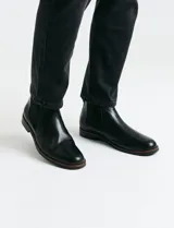 Bota tipo Chelsea de cuero negro con paneles elásticos laterales, suela de goma con detalle de vira en contraste y tirador trasero.