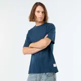 Remera de algodón color azul, de corte holgado, mangas cortas y cuello redondo. Cuenta con una pequeña etiqueta blanca decorativa en el borde inferior izquierdo.
