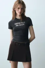 Camiseta de corte slim fit y efecto lavado color negro, con cuello redondo, manga corta y detalle de texto frontal con aplicación de brillos.