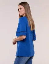 Remera de algodón azul con escote redondo y pequeña abertura central en V. Cuenta con mangas de largo intermedio decoradas con una inserción horizontal de puntilla calada y tajos laterales en el ruedo.