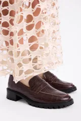Mocasines negros de estilo clásico con textura de cuero grabado tipo cocodrilo. Presentan una banda frontal característica y suela plana con borde definido.