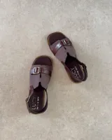 Sandalias marrones con tiras anchas de tela y cuero sintético, hebilla metálica y suela plana.