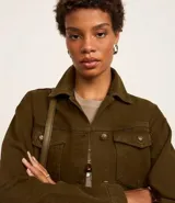 Campera trucker color verde oliva confeccionada en sarga de algodón, con cuello inglés, manga larga, bolsillos delanteros con solapa y abotonado delantero.