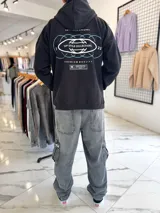 Canguro oversize negro con capucha y bolsillo tipo canguro. Presenta el texto "TOP STYLE COLLECTIONS" en el pecho y un estampado gráfico en la espalda con óvalos y texto en tonos celestes y blancos.