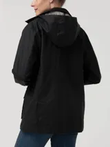 Chaqueta de algodón orgánico encerado, resistente al agua y al viento, con diseño de corte recto. Presenta cuello alto, gorro removible con forro a cuadros, cierre frontal metálico oculto por solapa con botones a presión y dos bolsillos frontales con solapa. Incluye detalles en cotelé y forro interior funcional.