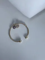 Pulsera tipo esclava de acero quirúrgico color dorado, con extremos esféricos y dijes colgantes: un círculo con strass y un dije de ojo turco con piedras azules y strass.