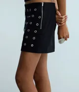 Short pollera corto de bengalina, con diseño ajustado y detalle de ojalillos metálicos distribuidos por toda la prenda. Cuenta con cierre lateral invisible.