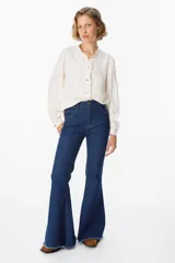 Camisa de manga larga color azul, con cuello mao y detalle de volados en la botonadura frontal. Presenta puños abotonados y un corte recto y fluido.