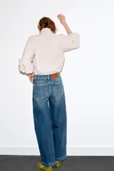 Jeans de tiro alto con corte culotte y pernera ancha. Presenta bolsillos de plastrón en el frente con detalle de pespuntes decorativos en forma de onda y costuras verticales a lo largo de la pierna. Cierre frontal con cremallera y botón metálico.
