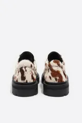 Zapato de cuero con acabado de pelo y estampado animal print tipo vaca, con punta redonda, cierre de cordones y suela track de goma negra.