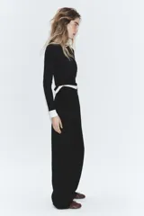 Pantalón negro de tiro alto, con trabillas, bolsillos laterales y de vivo en la espalda. Presenta pliegues en el delantero y cierre frontal con botón.