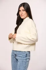 Buzo tejido de punto en color blanco crema, con cuello redondo alto y mangas largas con puños acanalados.