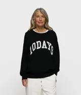 Suéter de punto negro con cuello redondo y corte holgado. Presenta el logotipo "10DAYS" bordado en blanco en el pecho con tipografía universitaria.
