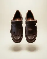 Mocasín de cuero natural color marrón chocolate, con costuras visibles, hebilla lateral metálica y solapa con flecos desmontable.