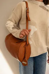 Cartera cilíndrica de cuero color suela, con cierre superior y correa larga ajustable.