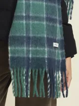Bufanda de tejido suave con diseño de cuadros escoceses en tonos verdes, azules y blancos. Presenta flecos en los extremos y una etiqueta de la marca en el lateral.