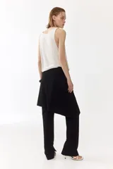 Pantalón recto de color negro con pollera mini superpuesta de corte asimétrico y cierre oculto lateral.