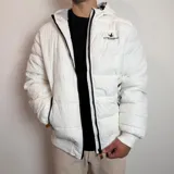 Campera puffer blanca con capucha, cierre frontal negro y puños de tejido elástico. Presenta el logo de Santa Barbara Outfitters bordado en el pecho.