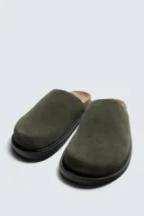 Zueco cerrado de hombre, color verde militar, fabricado en piel con acabado serraje (gamuza). Presenta plantilla acolchada y suela de goma negra con volumen.