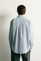 Camisa de corte regular fit confeccionada en algodón, con estampado de cuadros pequeños en tonos celestes. Presenta cuello abotonado, cierre frontal con botones y mangas largas con puños abotonados.