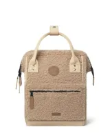 Mochila Cabaia modelo Adventurer Manchester, confeccionada en tejido tipo corderito color beige. Presenta asas superiores y detalles en cuero sintético color crema, bolsillo frontal con cierre y parche de la marca en el centro.