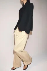 Pantalón de tiro medio con corte wide leg, confeccionado en algodón. Presenta cintura con trabillas, bolsillos laterales ocultos y detalle de pliegues en el delantero. Cierre frontal con cremallera, botón y ganchos metálicos.