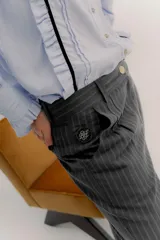 Pantalón sastrero de tiro medio, color gris oscuro con rayas verticales finas. Presenta pinzas delanteras, bolsillos delanteros con pin bordado y bolsillos traseros tipo vivo.